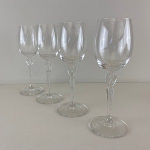 Op de afbeelding: Vier heldere glazen wijnglazen met een decoratief steelontwerp. De glazen zijn in een rij op een wit oppervlak gerangschikt.