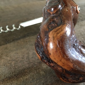 May include: A wooden corkscrew with a silver metal worm. The wood is dark brown and has a natural, rustic look.