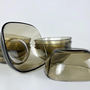 Op de afbeelding: Set van zes heldere bruine glazen kommen. De kommen zijn vierkant en hebben een afgeronde bodem. De kommen zijn op elkaar gestapeld.