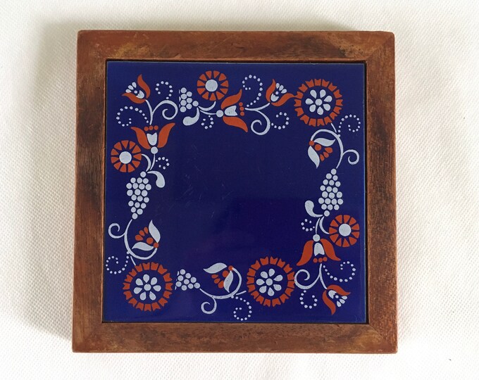 A vintage trivet or dish stand made from a ceramic bleu tile and a wooden frame