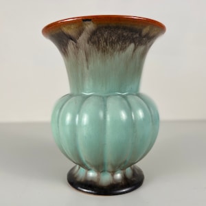 Op de afbeelding: Een kleine, lichtblauwe keramische vaas met een geribbeld lichaam en een bruine rand. De vaas heeft een gemarmerde glazuur met bruine en groene accenten.