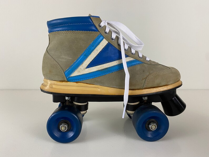 May include: A pair of vintage roller skates with a gray suede upper, blue and white accents, and white laces. The skates have black wheels with blue rims.