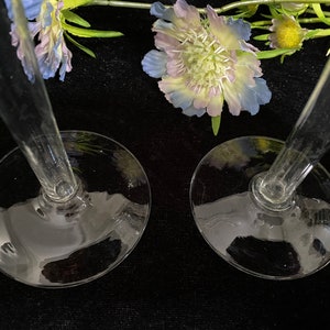 May include: Two clear glass candle holders with a wide base and a tall, slender stem. The candle holders are on a black surface.