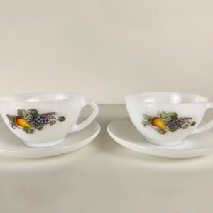 May include: Two white ceramic teacups with matching saucers. Each cup features a simple design of a pear and grapes on a vine.