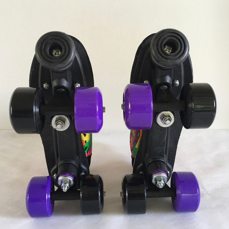 May include: Pair of black roller skates with purple wheels and colorful graphics on the sides. The skates have a black metal frame and a black plastic base.