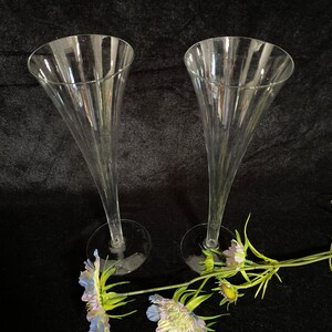 May include: Two clear glass champagne flutes on a black background with a sprig of blue and green flowers.