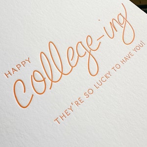 K&ouml;nnte beinhalten: Eine wei&szlig;e Karte mit dem Text "Happy college-ing. They're so lucky to have you!" in orangefarbener Schrift.