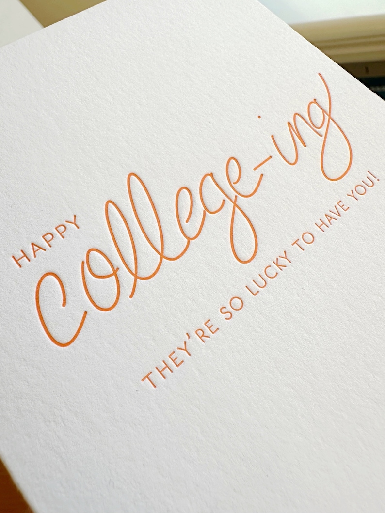 K&ouml;nnte beinhalten: Eine wei&szlig;e Karte mit dem Text "Happy college-ing. They're so lucky to have you!" in orangefarbener Schrift.