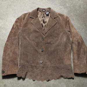 以下が含まれることがあります： ノッチカラーと3つボタンの留め具が付いた茶色のスエードブレザー。ジャケットはスカラップの裾と長袖が特徴です。ブレザーはニュートラルカラーで、さまざまな場面に適しています。