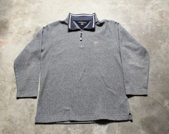 May include: A gray long-sleeve pullover with a quarter-zip neckline. The collar is navy blue with white trim. A small logo is visible on the chest. The shirt is made of a textured fabric.