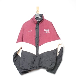 Puede incluir: Chaqueta burdeos, negra y blanca con botones y cuello alzado. La chaqueta tiene un logotipo en el pecho y la palabra "UMBRO" en la parte superior izquierda. La chaqueta está colgada de una percha de madera.