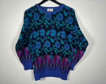 May include: A blue, green, black, and pink patterned sweater with a crew neck. The sweater has a floral design and a geometric pattern at the bottom. The brand label reads "keren".