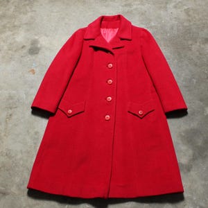 May include: A vibrant red coat with a classic design. The coat features a collared neckline, long sleeves, and a button-down front. Two flap pockets are placed on the front. The coat is made of a soft material.