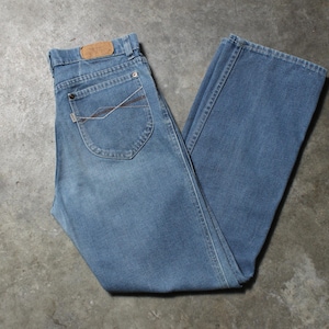 May include: Light blue denim jeans with a classic five-pocket design. The jeans have a straight leg cut and a brown leather patch on the back. The jeans are folded and laid flat on a concrete surface.