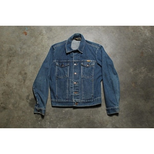 May include: A medium-wash blue denim jacket featuring a pointed collar, long sleeves with buttoned cuffs, and a front button closure. The jacket includes two chest pockets with buttoned flaps and vertical seam detailing along the front torso.
