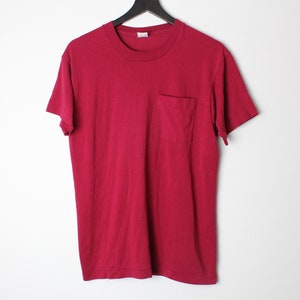 May include: A plain red t-shirt with a single pocket on the left side.
