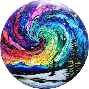 Op de afbeelding: Een ronde, kleurrijke decoratie met een glas-in-loodstijl ontwerp. Het kunstwerk toont een wervelende aurora borealis met levendige tinten rood, roze, groen en blauw. De onderkant toont een besneeuwd landschap met dennenbomen.