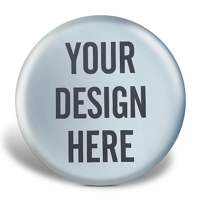 Op de afbeelding: Een ronde, lichtblauwe knoop met de tekst "YOUR DESIGN HERE" in donkergrijs. De knoop heeft een glanzende afwerking en een subtiele schaduw, wat een driedimensionaal effect suggereert. Ideaal voor gepersonaliseerde ontwerpen.