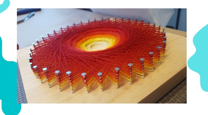 Pode incluir: Uma pe&ccedil;a circular de arte de corda com um degradado de fio vermelho, laranja e amarelo enrolado em torno de pregos martelado em uma t&aacute;bua de madeira.