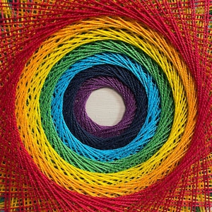 Pode incluir: Um design de arte de barbante arco-&iacute;ris com um padr&atilde;o circular. A arte de barbante &eacute; feita com barbante colorido e pregos martelado em uma t&aacute;bua de madeira.