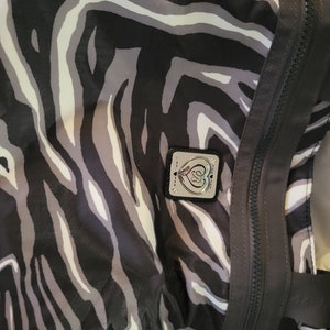 May include: A black and white zebra print tote bag with a silver heart logo. The bag has a zipper closure and a top handle.