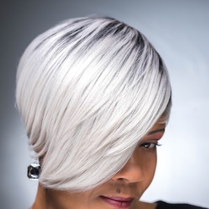 May include: A woman with short, silver-grey hair styled in a pixie cut. She is wearing a black top and a silver necklace with a heart pendant.