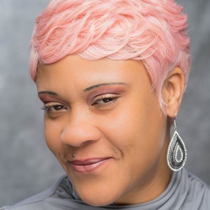 Può includere: Una donna con capelli corti rosa e una maglia grigia. Sta guardando in basso e sorridendo.