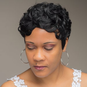 May include: A woman with short, curly black hair and silver hoop earrings. She is wearing a white lace top and has her eyes closed.