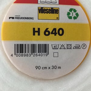 Könnte beinhalten: Eine gelbe und rote Rolle Vlieseline H 640 Bügelvlies, eine Marke von Freudenberg. Die Rolle ist 90 cm x 30 m groß. Das Etikett enthält einen Barcode, Waschanweisungen und ein Recycling-Symbol.