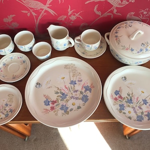 May include: A set of white ceramic dishes with a floral pattern featuring blue, pink, and green flowers. The set includes a large serving dish, two smaller plates, a creamer, and four teacups with saucers.
