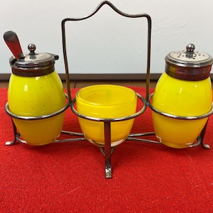 May include: A silver condiment set with three yellow glass containers. The set has a metal stand with a handle.
