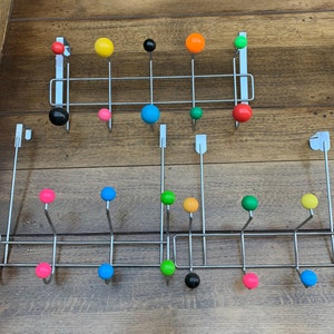 May include: A set of two metal coat racks with colourful round knobs. The top rack has black, yellow, orange, red, and green knobs. The bottom rack has pink, blue, green, yellow, and black knobs.