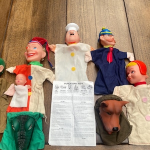 May include: A set of seven colourful hand puppets, including a chef, a clown, a sailor, a baby, a dog, and two others. The puppets are made of felt and have embroidered features. The set also includes a card with the text "Punch and Judy".