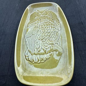 May include: A rectangular ceramic tray with rounded corners, glazed in a glossy olive green finish. The center features a raised, molded relief of an owl perched on a branch, with detailed feather textures and a smooth, reflective surface.