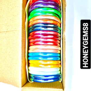 May include: A box of colorful plastic bangles. The bangles are stacked in a box and are arranged in a rainbow pattern. The box is open and the bangles are visible. The text "HONEYGEMS8" is printed on the side of the box.