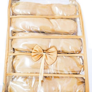 May include: A clear plastic storage bag with a brown fabric exterior and a satin bow. The bag has multiple compartments for storing items like scarves, ties, or belts.