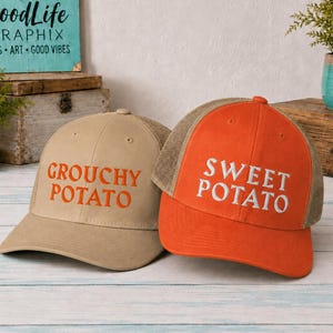 May include: Two baseball caps with mesh backs. One cap is tan with orange text that reads GROUCHY POTATO. The other cap is orange with white text that reads SWEET POTATO. Both caps feature a structured front panel and a curved brim design.