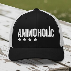 Peut inclure: Casquette de camionneur noire et blanche avec le mot "AMMOHOLIC" brodé en blanc, accompagné de quatre étoiles blanches. La casquette a une visière noire et un dos en filet blanc.