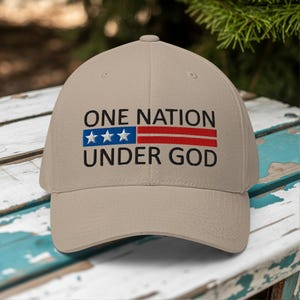 May include: A tan baseball cap with the text "ONE NATION UNDER GOD" embroidered in black. The design includes a blue rectangle with three white stars and red stripes, resembling the American flag.