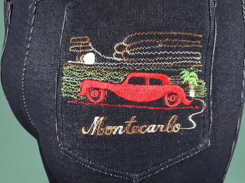 May include: Dark blue denim jeans with an embroidered pocket. The embroidery depicts a red vintage car, palm tree, and the word "Montecarlo" in gold thread. The design is detailed and colourful, adding a unique element.