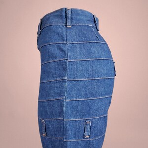 K&ouml;nnte beinhalten: Ein Jeansrock mit einem einzigartigen Design. Der Rock besteht aus horizontalen Denimstreifen, die einen geschichteten Effekt erzeugen. Er hat G&uuml;rtelschlaufen und kleine Taschen. Der Jeansstoff hat eine mittelblaue Waschung.