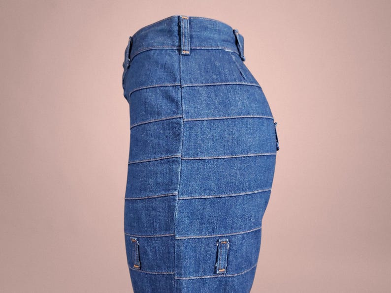 K&ouml;nnte beinhalten: Ein Jeansrock mit einem einzigartigen Design. Der Rock besteht aus horizontalen Denimstreifen, die einen geschichteten Effekt erzeugen. Er hat G&uuml;rtelschlaufen und kleine Taschen. Der Jeansstoff hat eine mittelblaue Waschung.
