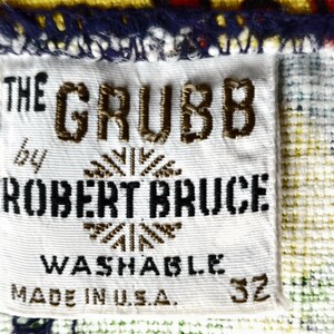 Peut inclure: Gros plan sur une &eacute;tiquette en tissu blanc avec le texte "THE GRUBB by ROBERT BRUCE WASHABLE MADE IN U.S.A. 32" en lettres marron et noires. L'&eacute;tiquette est cousue sur un tissu &agrave; motifs bleu, jaune, vert et blanc.