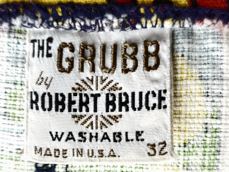 Peut inclure: Gros plan sur une &eacute;tiquette en tissu blanc avec le texte "THE GRUBB by ROBERT BRUCE WASHABLE MADE IN U.S.A. 32" en lettres marron et noires. L'&eacute;tiquette est cousue sur un tissu &agrave; motifs bleu, jaune, vert et blanc.