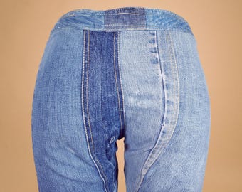 May include: Close-up of denim pants with a patchwork design. The pants feature a combination of light and dark blue denim panels, with visible stitching. The design includes a central vertical panel of darker denim.