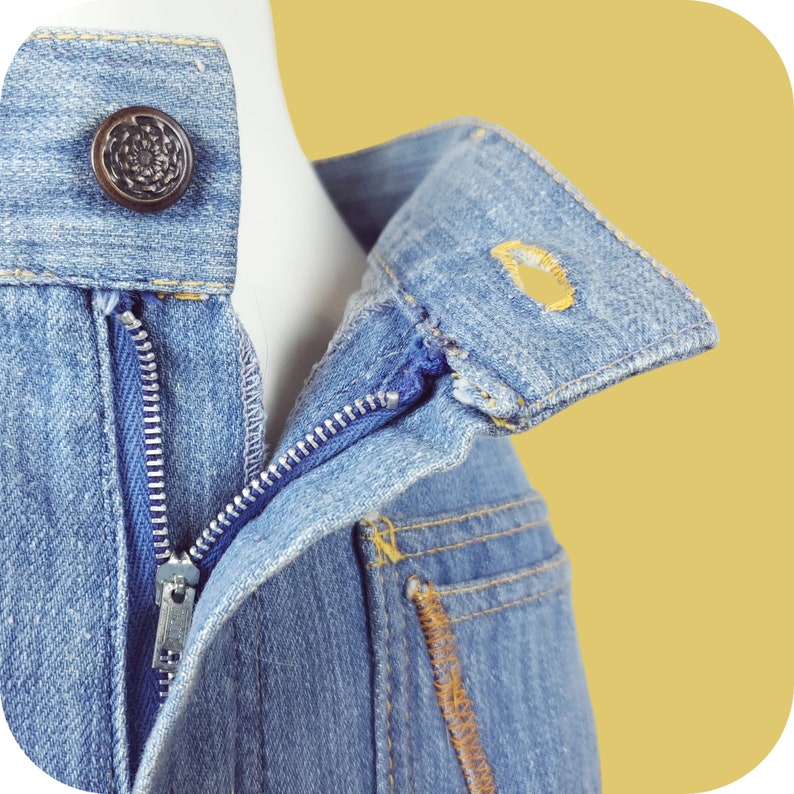K&ouml;nnte beinhalten: Nahaufnahme einer blauen Jeansjacke mit Rei&szlig;verschluss und Knopfverschluss. Die Jacke hat einen Kragen und eine Tasche auf der Vorderseite.