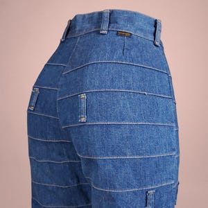 K&ouml;nnte beinhalten: Nahaufnahme einer blauen Jeans mit horizontalen Steppdetails. Die Jeans hat ein klassisches F&uuml;nf-Taschen-Design und ein Wrangler-Etikett am Bund. Die Jeans ist aus mittelblauem Denim.