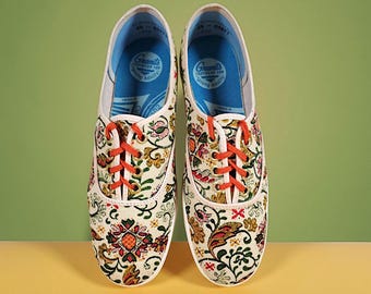 Könnte beinhalten: Paar Leinenschuhe mit floralem Muster und orangefarbenen Schnürsenkeln. Die cremefarbenen Schuhe weisen ein Muster aus Blumen und Blättern auf. Der Innenraum ist blau mit dem Text "Green's Footwear for Young Adults".