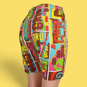 Peut inclure: Shorts color&eacute;s avec une taille &eacute;lastique. Ils pr&eacute;sentent un motif r&eacute;p&eacute;t&eacute; du mot "GRUB" dans diverses couleurs, dont le marron, le rose, le vert et le bleu, sur fond blanc. Les shorts sont faits d'un tissu l&eacute;ger.