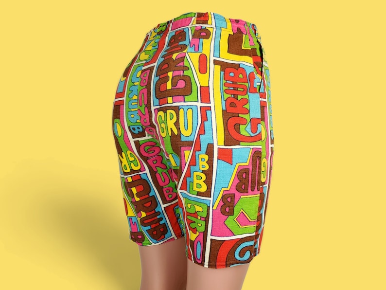 Peut inclure: Shorts color&eacute;s avec une taille &eacute;lastique. Ils pr&eacute;sentent un motif r&eacute;p&eacute;t&eacute; du mot "GRUB" dans diverses couleurs, dont le marron, le rose, le vert et le bleu, sur fond blanc. Les shorts sont faits d'un tissu l&eacute;ger.